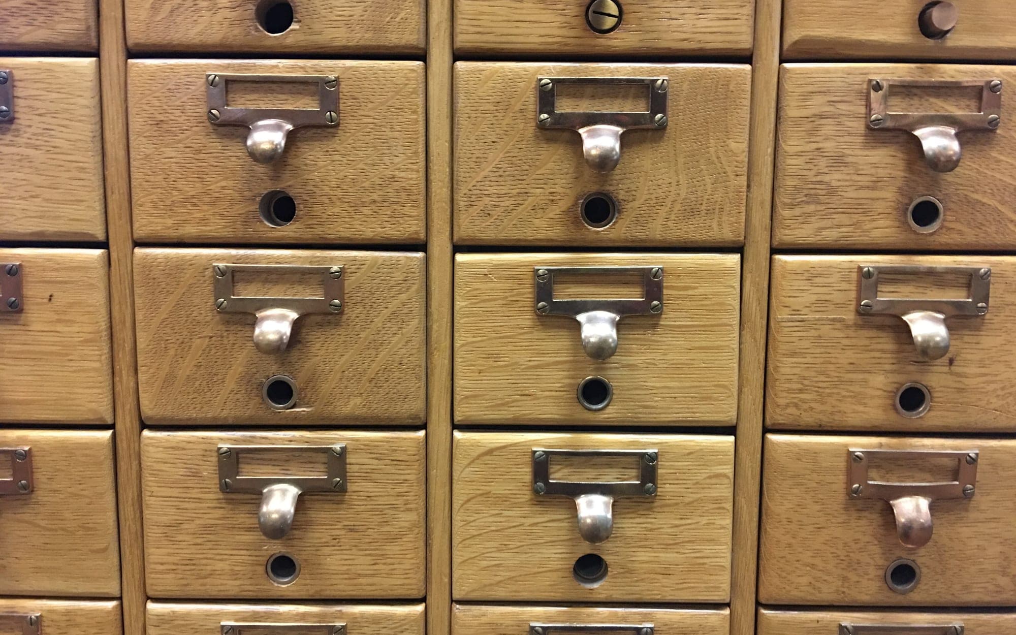 Rows of wooden library card catalog drawers with brass label holders and pull handles