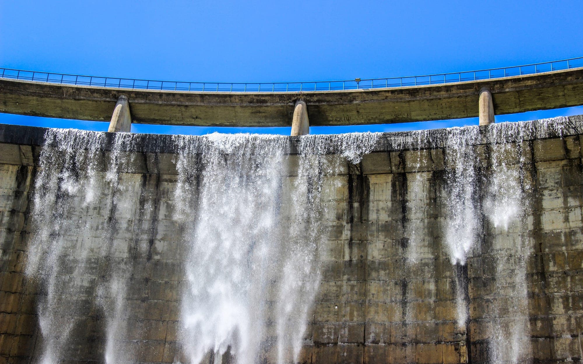 Water spilling over the crest of a concrete dam and running down its face in white streams