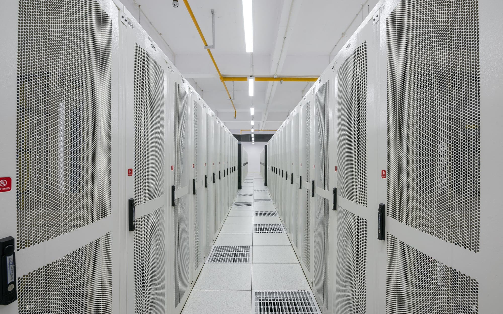 A straight aisle between rows of white server cabinets with perforated doors in a data center