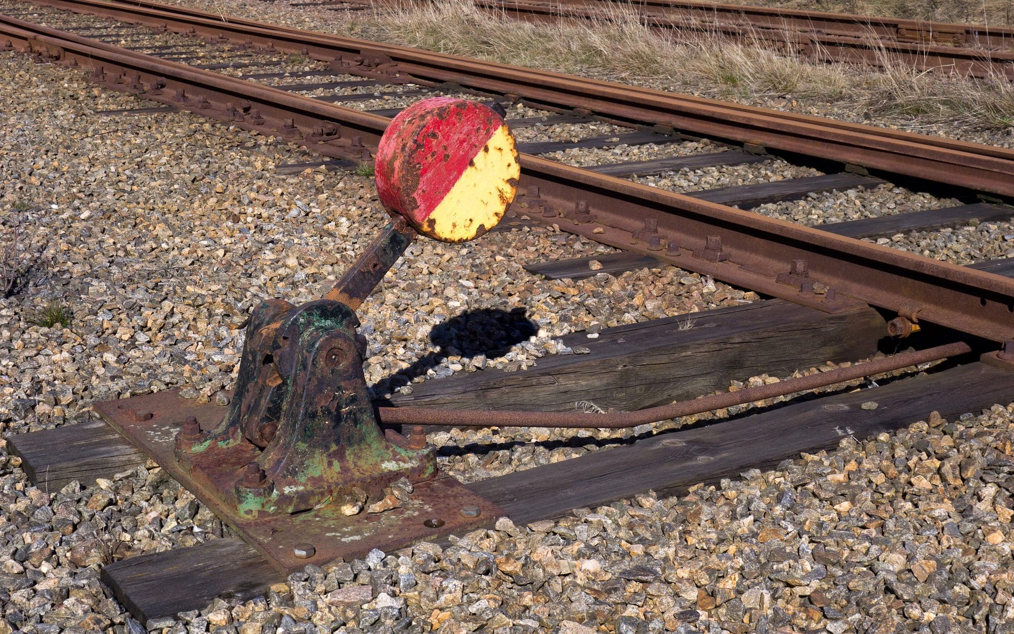 An old manual railway switch lever with a red and yellow disc beside rusty rails on a gravel bed
