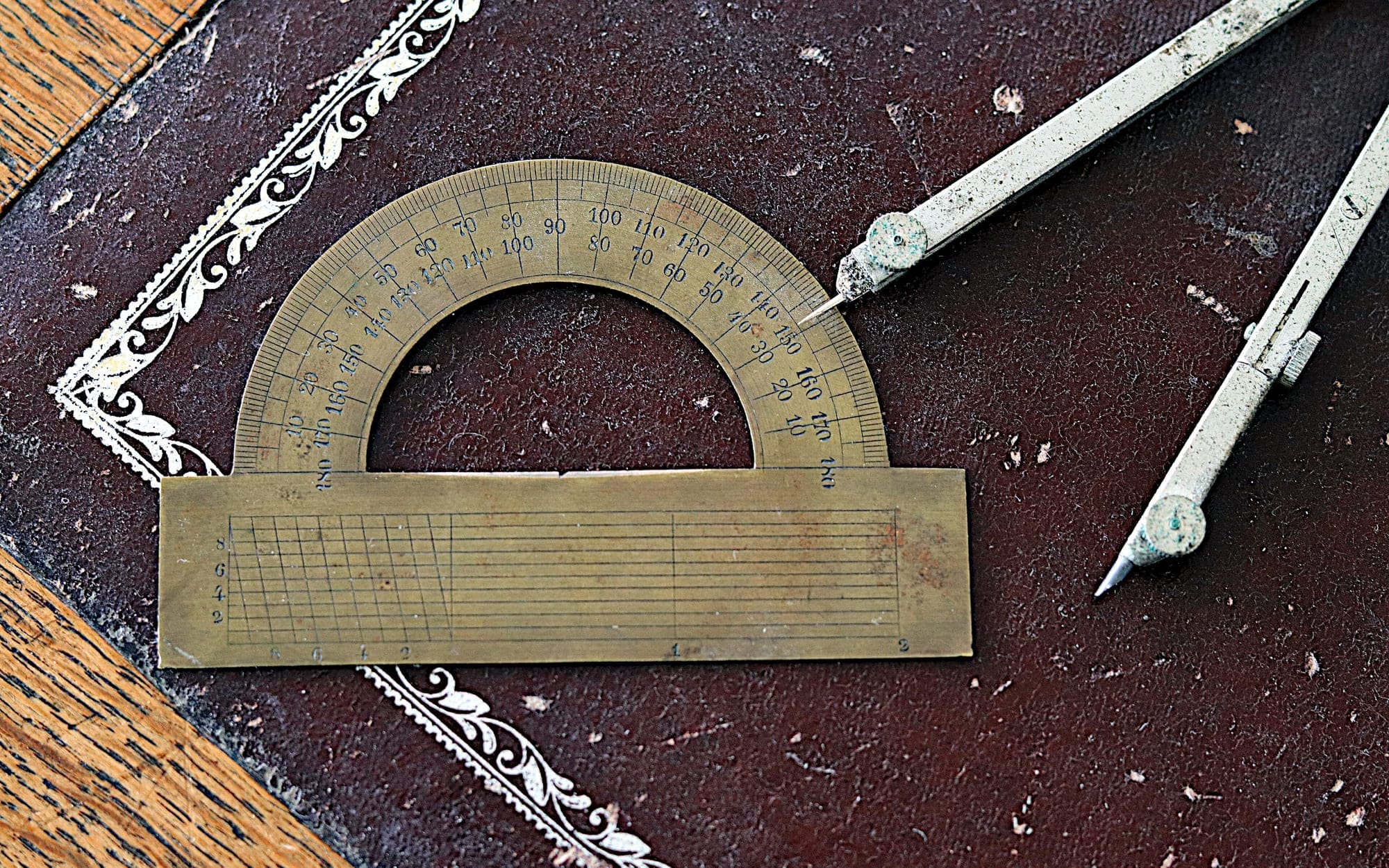 Antique brass protractor with a scale and a drawing compass on a dark leather surface
