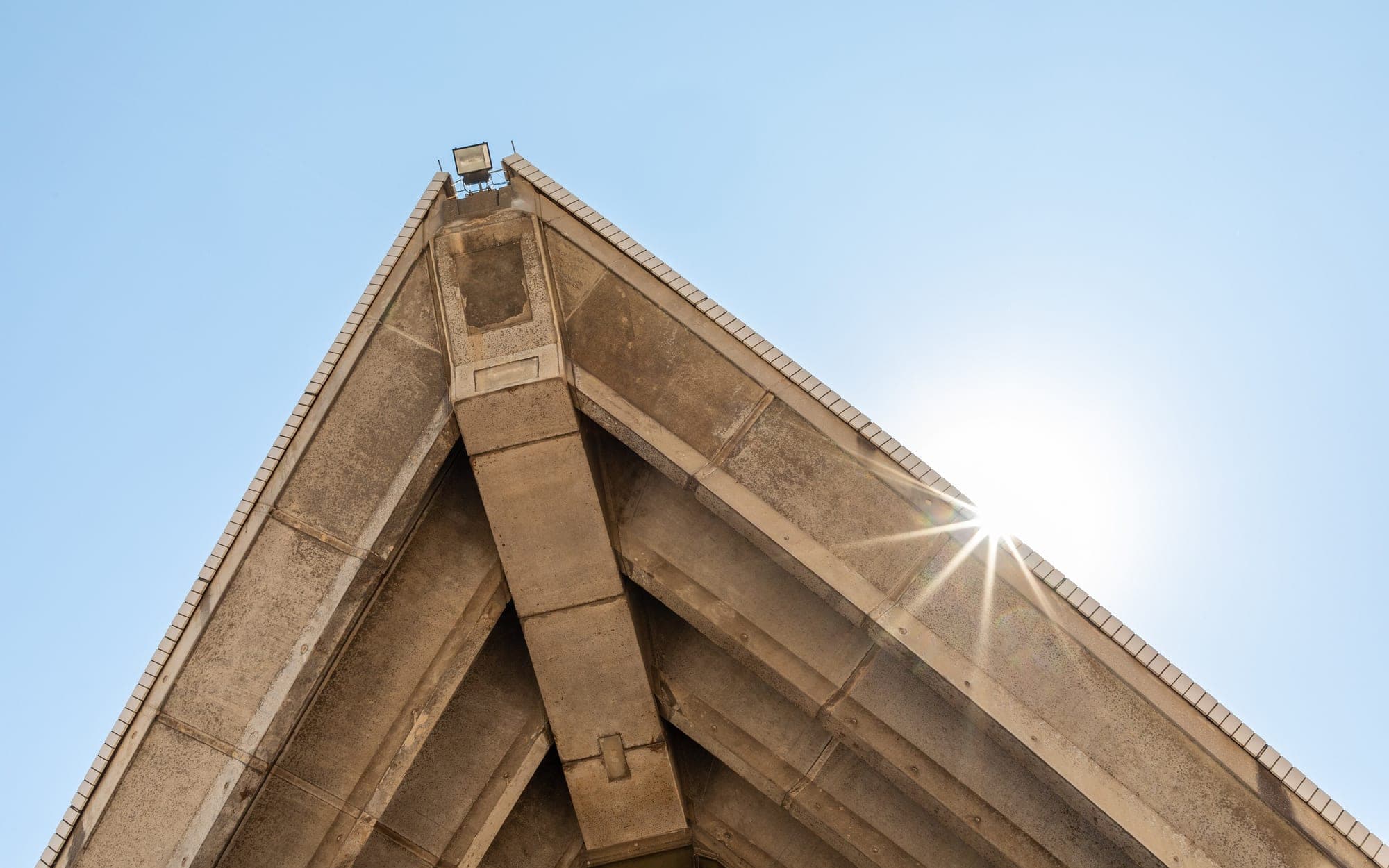 Underside of a concrete roof shell rib against a bright sky, with the sun behind its edge