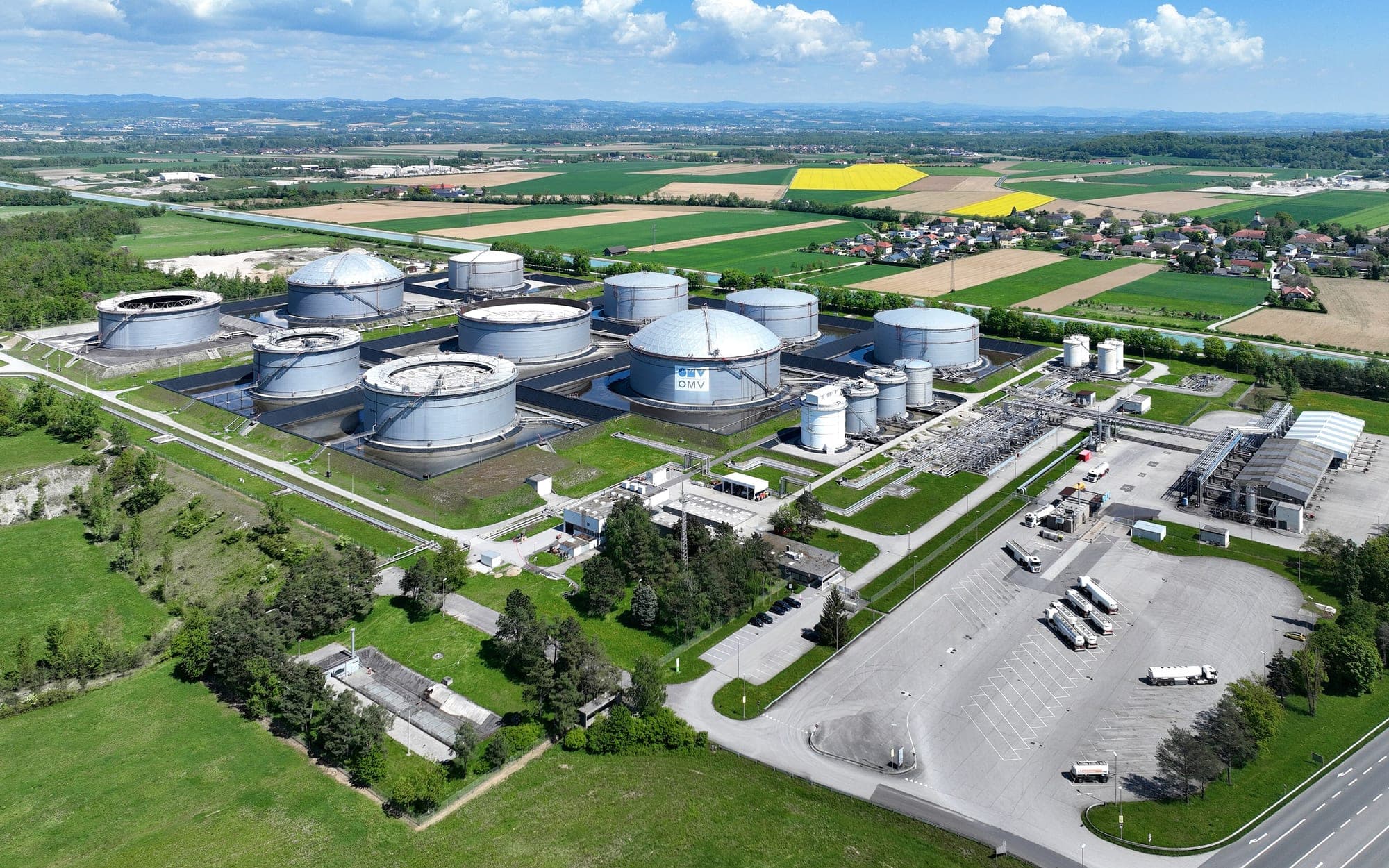 Aerial view of an oil tank farm with round storage tanks surrounded by fields and roads