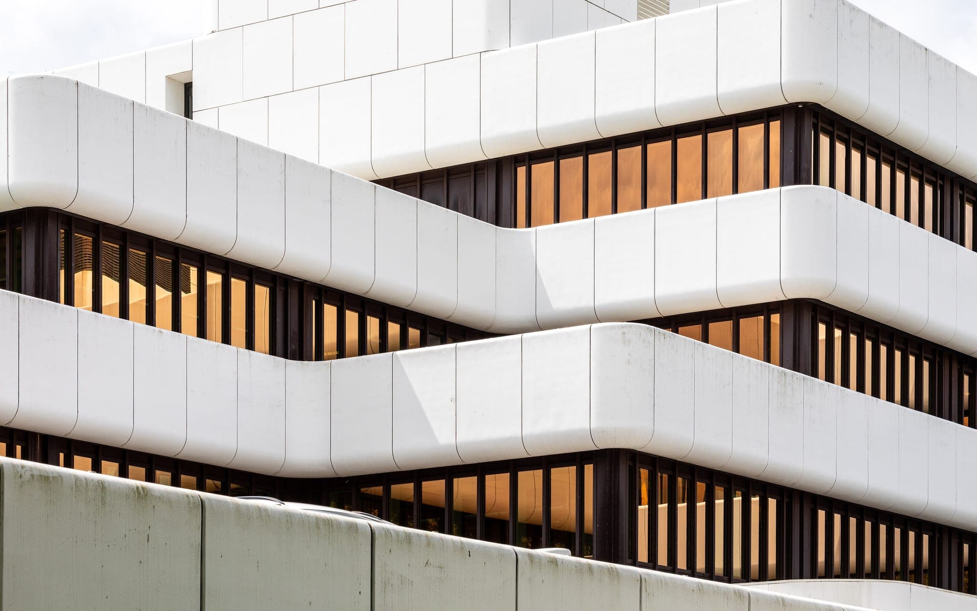 White horizontal bands on an office building facade alternate with rows of windows stacked in tiers