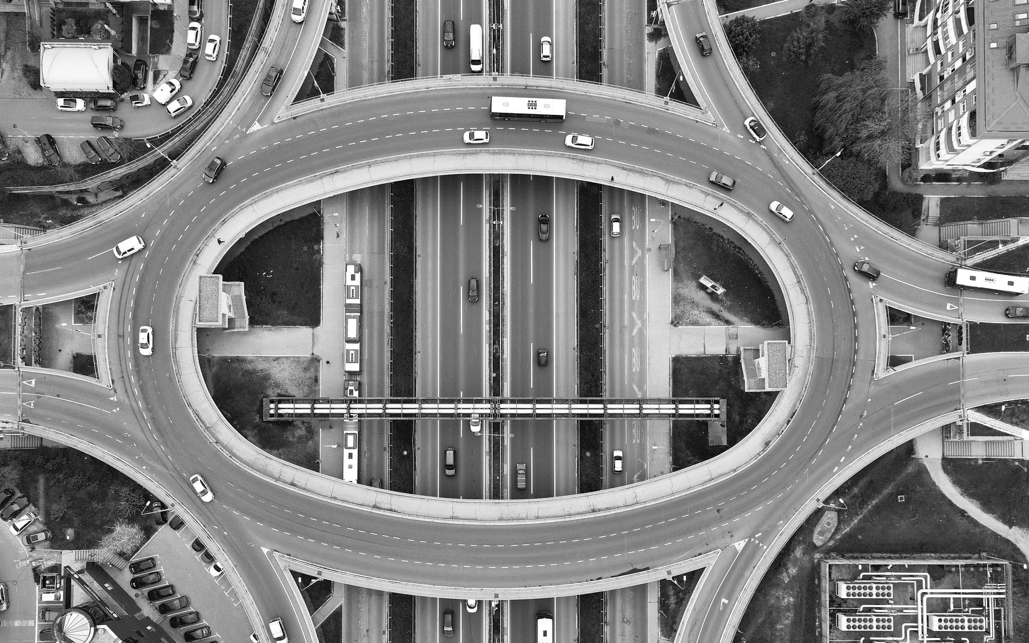 Black-and-white aerial view of an oval interchange above a multilane avenue with cars and buses
