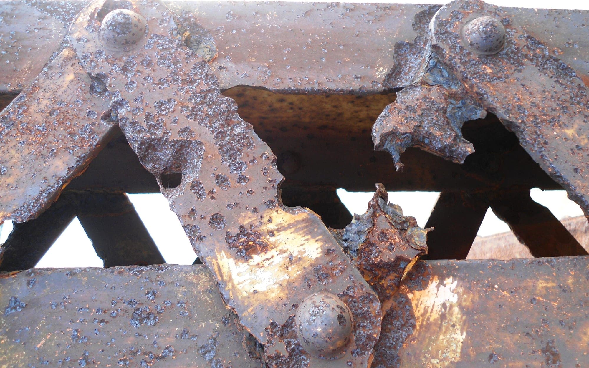 Close-up of heavily rusted riveted steel members in the lattice truss of an old bridge