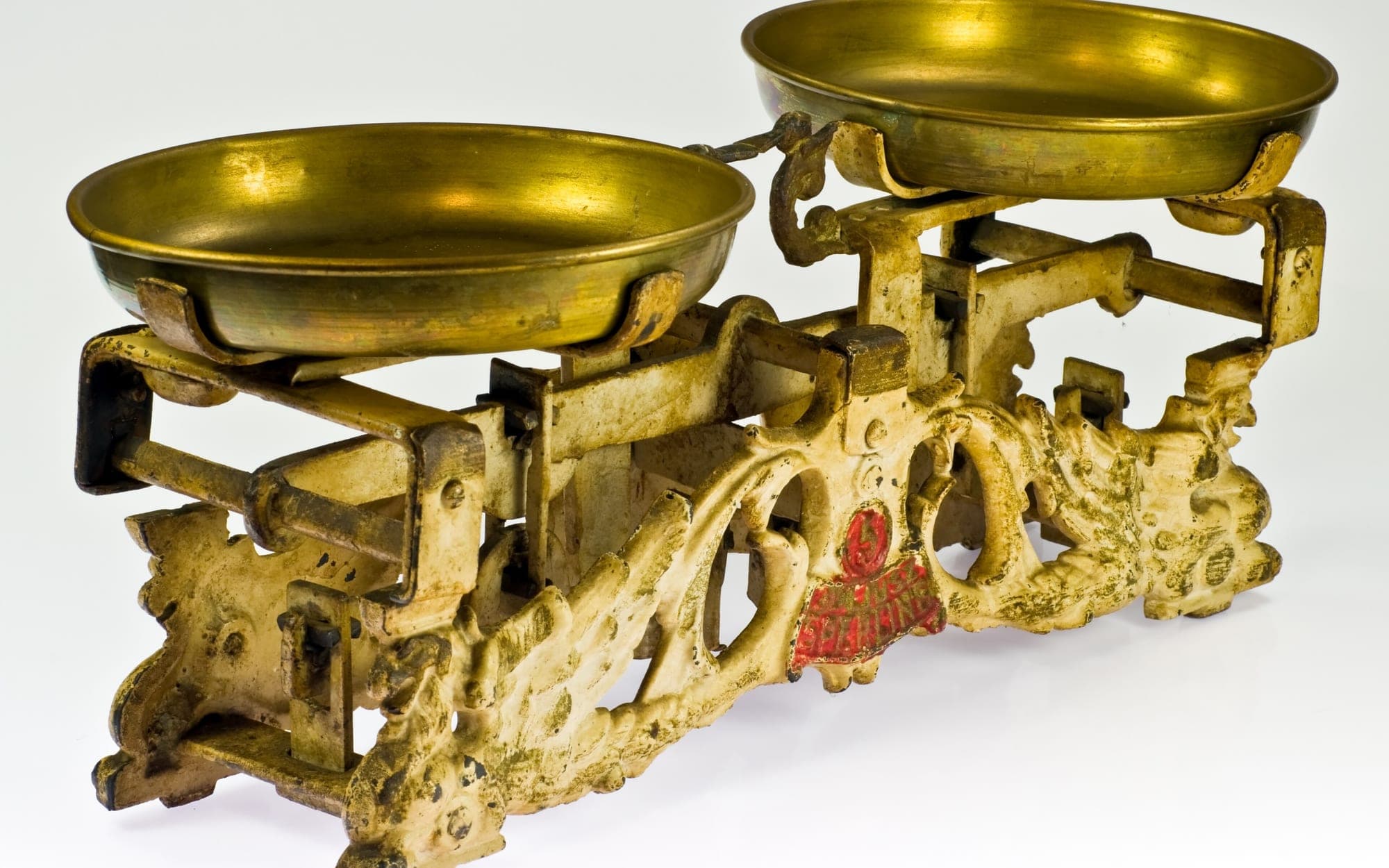 An antique cast-iron balance scale with two brass pans on a white background
